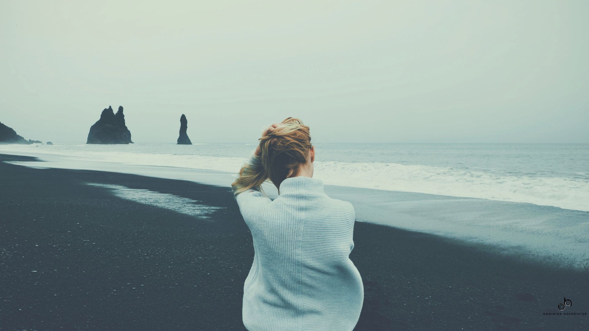 Eine Frau sitzt am Strand und schaut auf das Meer